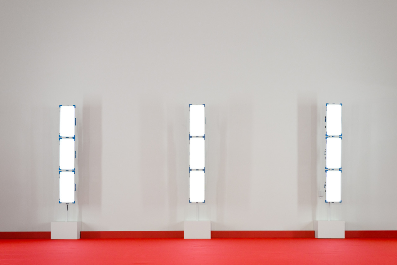 Empty runway set with three light towers against a white wall on a red carpet, before the show.