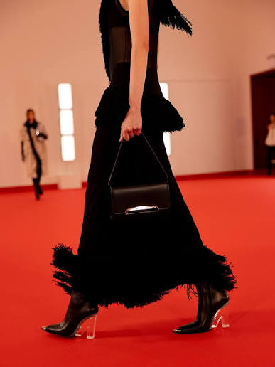 Close crop of a fringed black gown and handbag on the red carpet.