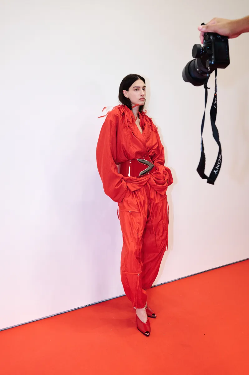 A guest backstage in a red belted jumpsuit, photographed by a Sony camera.