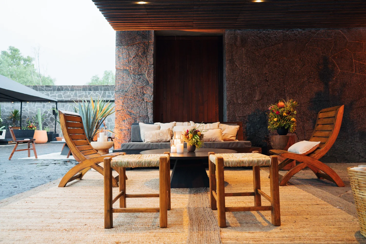 Teak lounge chairs and a low table with candles and a floral arrangement, set beneath the museum's dark stone archway.