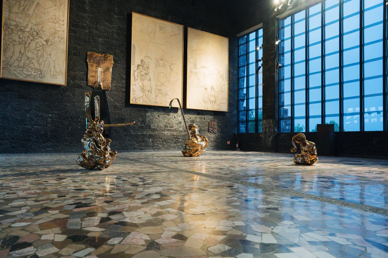 Bronze sculptures on a marble-tiled gallery floor, staged in front of large works on paper inside the museum.