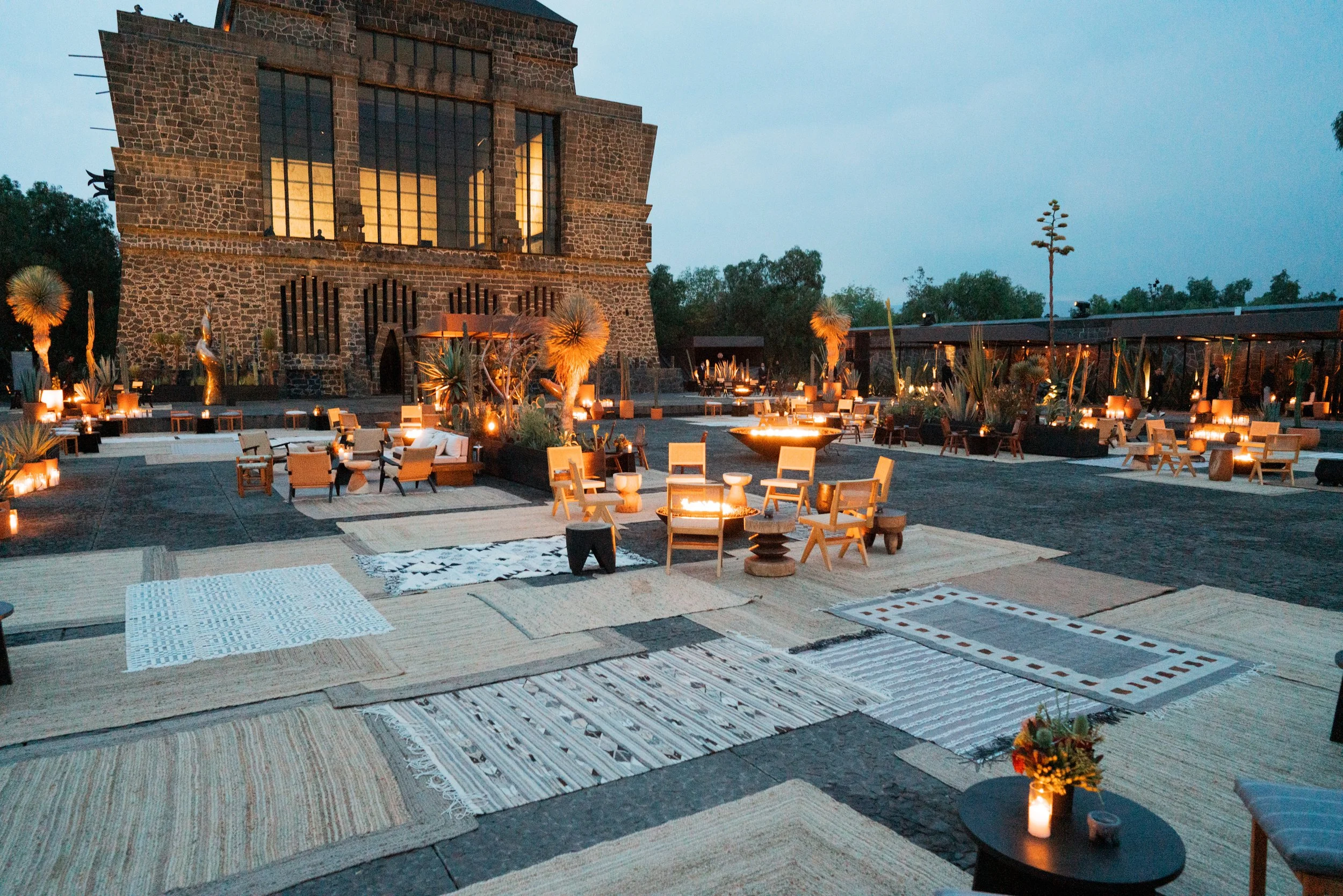 Wide dusk view of Museo Anáhuacalli's courtyard, lit windows and firelight spread across the whole plaza for the Dior Cruise Mexico welcome dinner.