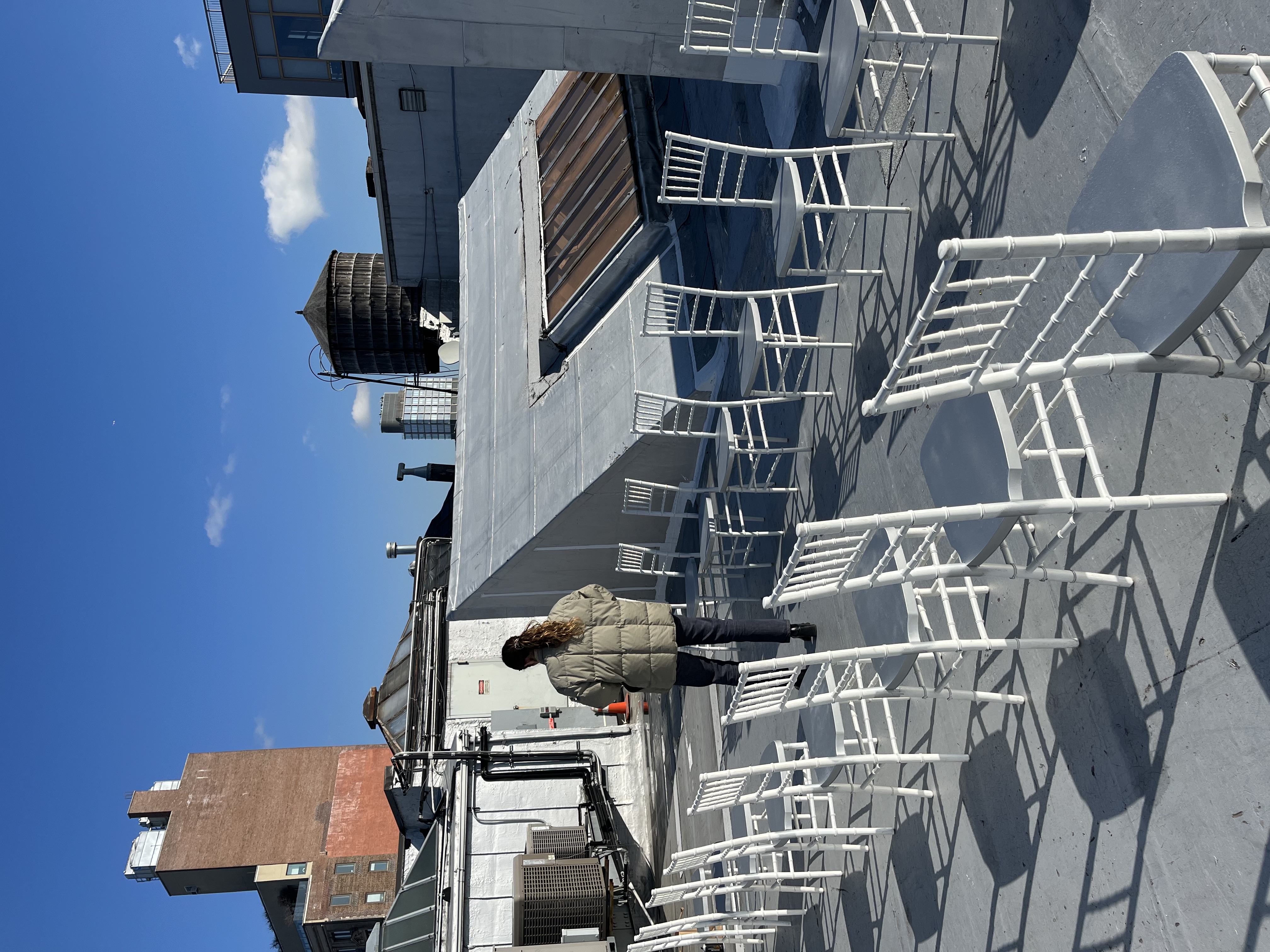 Rooftop covered in plastic sheeting with rows of white chiavari chairs, ahead of hand-glittering them for the show.