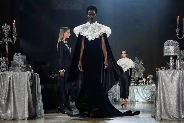 Models in black gowns with dramatic white lace collars walking the runway between glittered silver tablescapes.