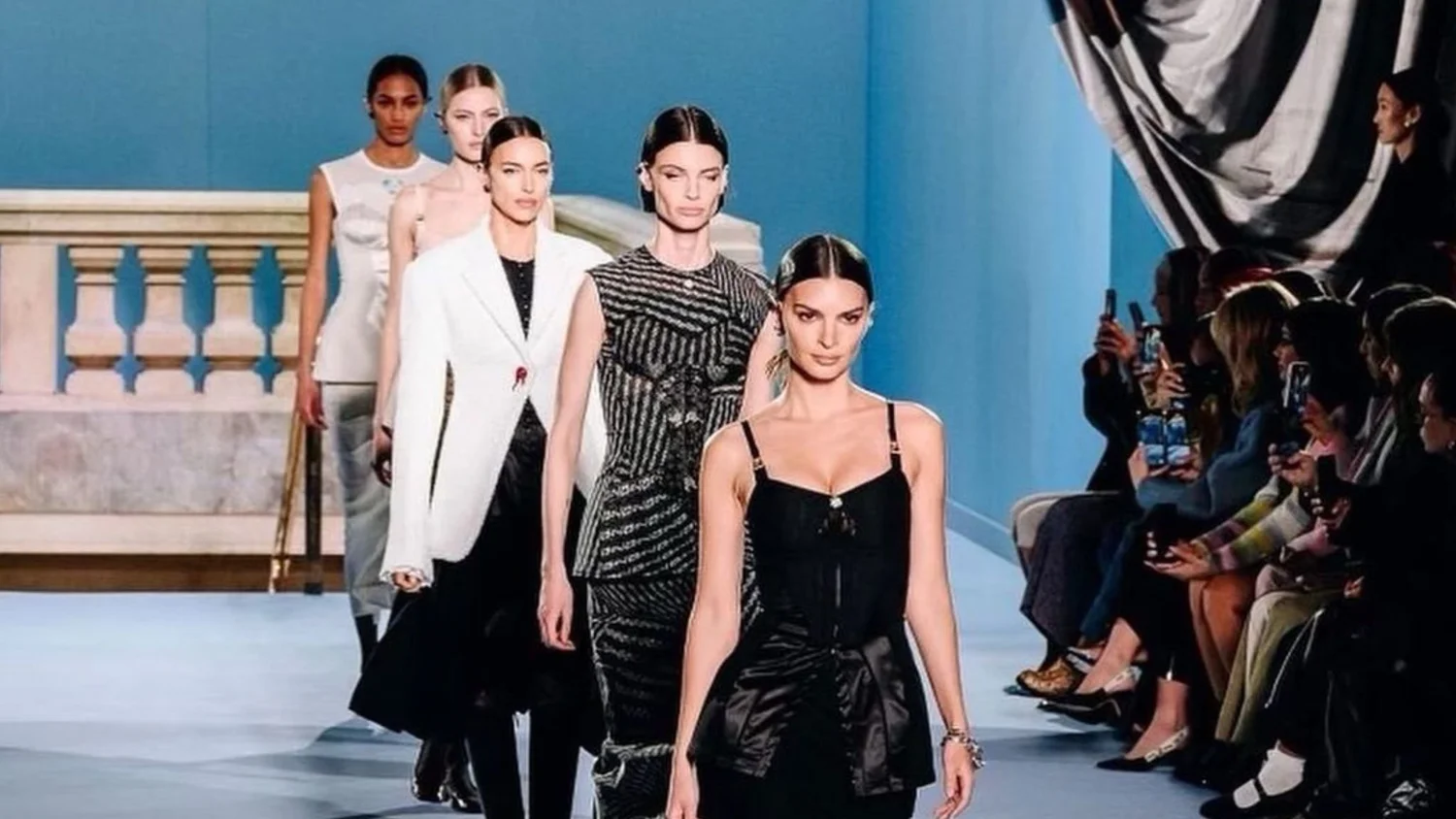 Models in black and white looks walking the runway past a seated front row.