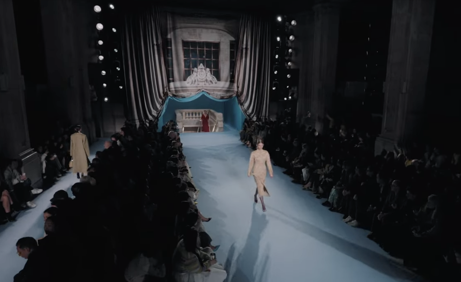Wide view of the runway and seating from above, with a model walking toward a staged alcove.