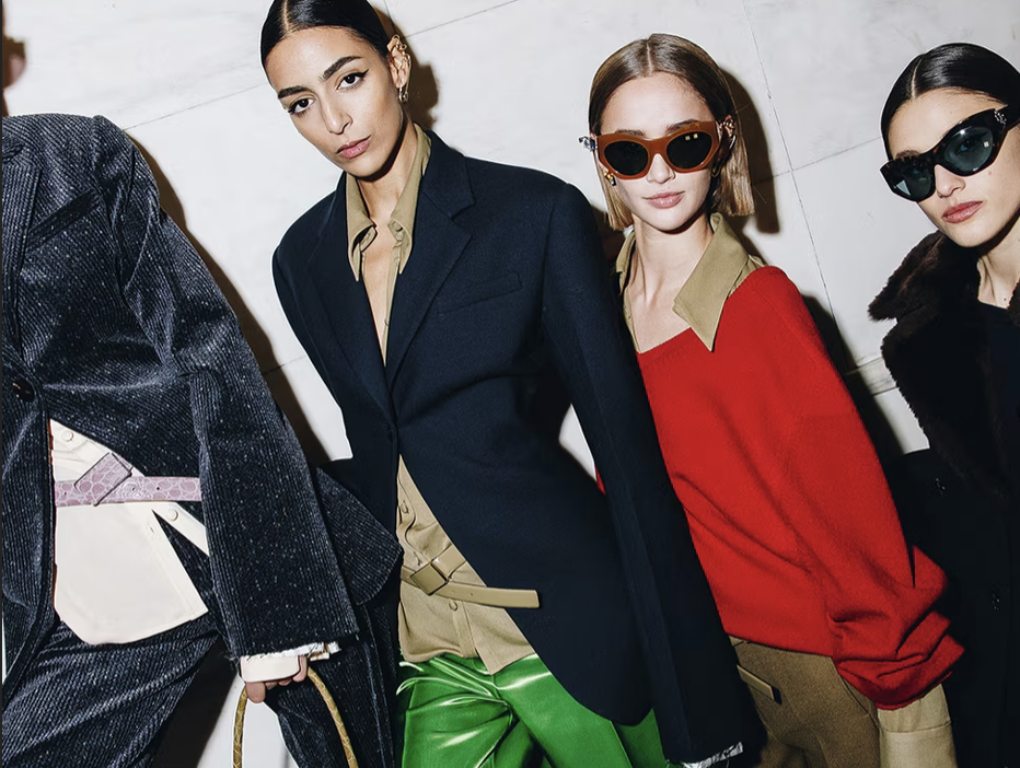 Group of models backstage in tailored looks and sunglasses.