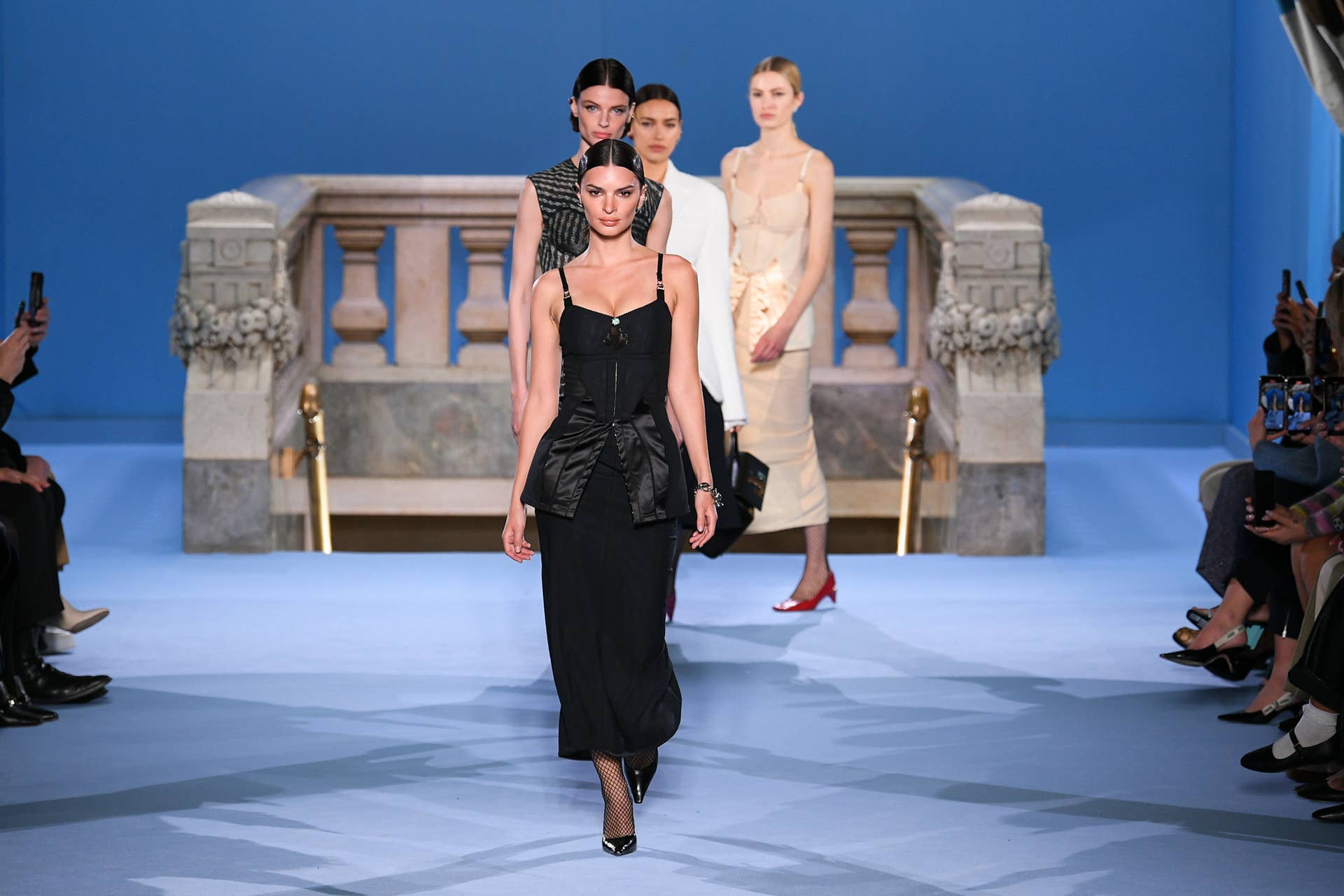Models walking the runway at the Tory Burch Fall/Winter 2023 show, with a marble balustrade set piece against a blue backdrop.