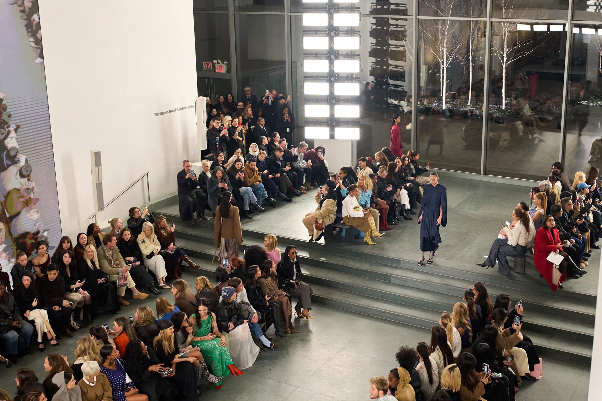Overhead view of the show in the Agnes Gund Garden Lobby, guests seated on tiered steps around the runway.